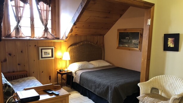 Un dormitorio acogedor con cama, lámpara de noche, cabecera de madera y una silla de mimbre.