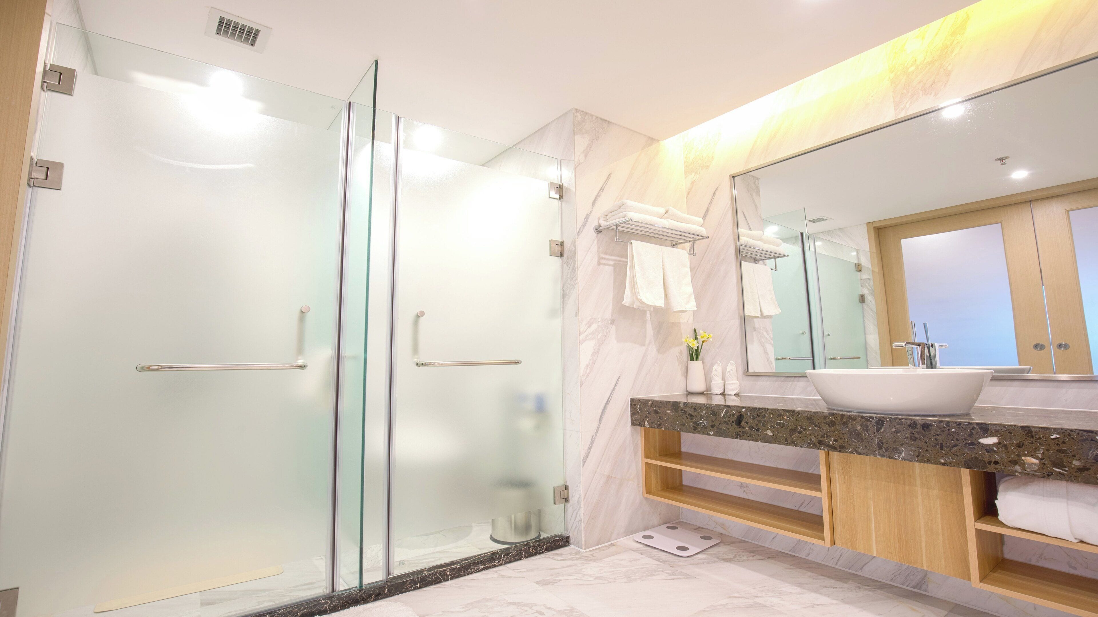 A modern bathroom with a glass-enclosed shower, a large mirror, and a marble-topped vanity.