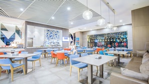 A modern restaurant interior with multiple dining tables and chairs, a kitchen area, and a large window with festive decorations.