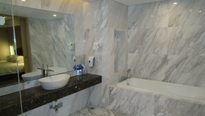 A modern bathroom with a large mirror, a sink, a bathtub, and a hairdryer mounted on the wall.
