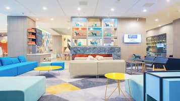 A modern lobby with seating areas, a reception desk, and a display wall with decorative items.
