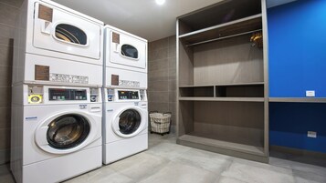 A laundry room with two stacked front-loading washing machines, a drying rack, and a blue wall.