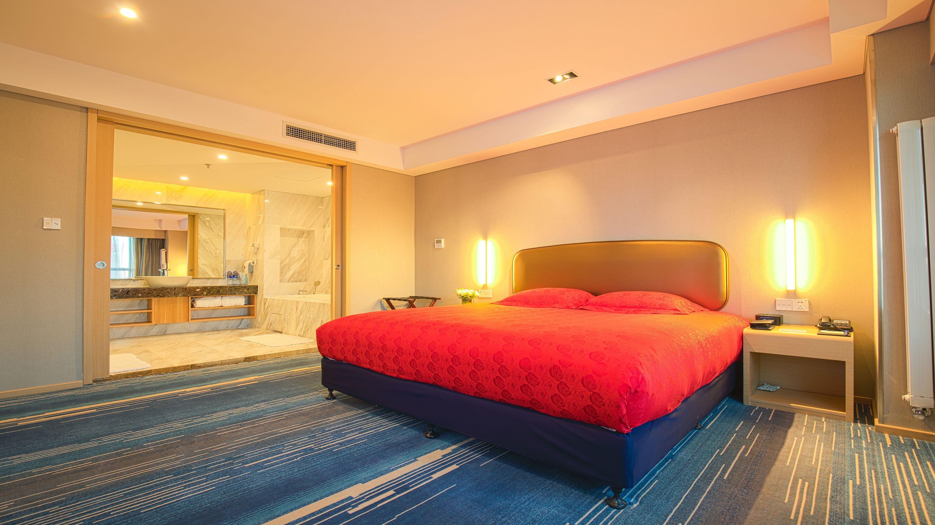 Habitación de hotel con una cama grande, baño con tocador de mármol y vista al pasillo.