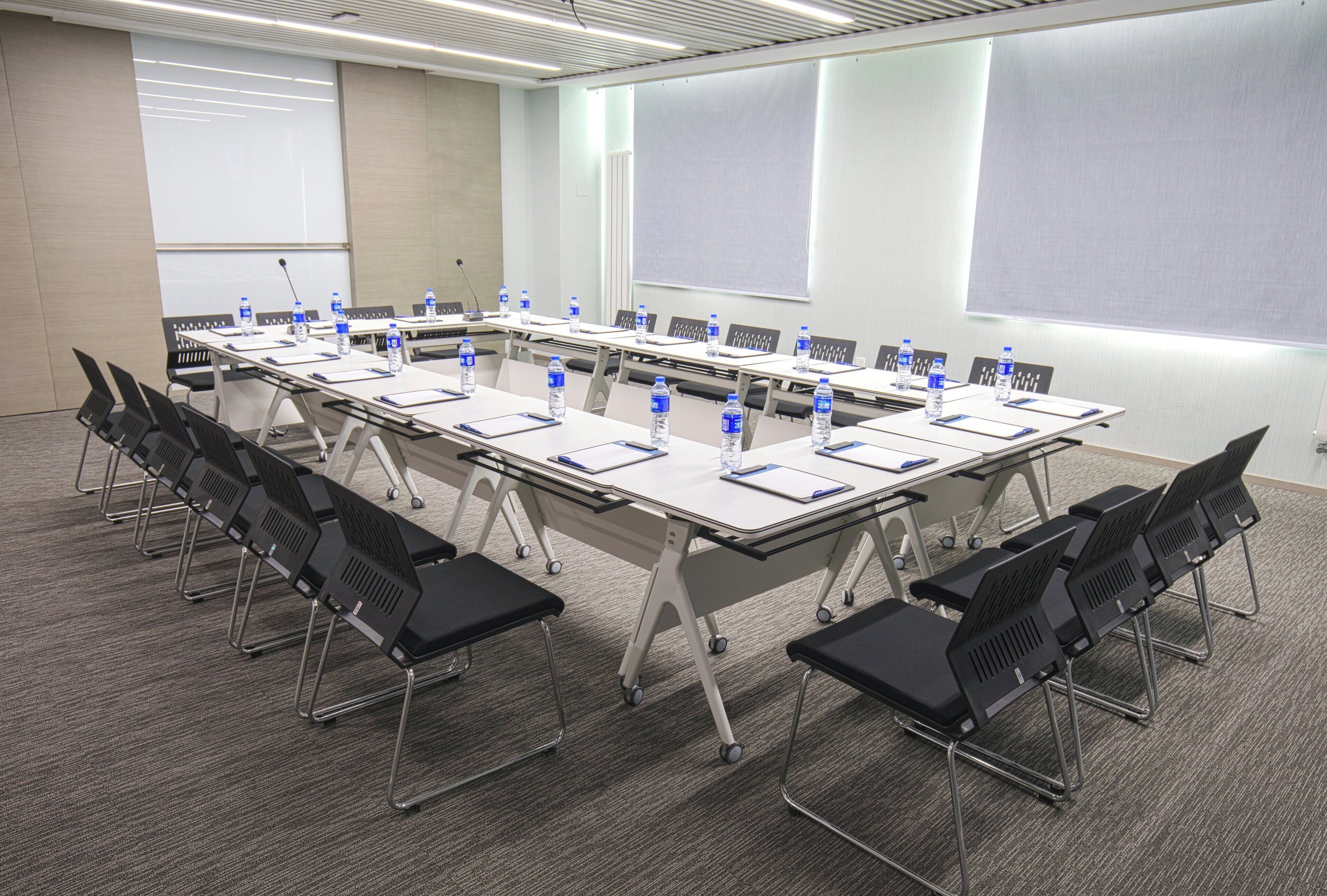 A conference room with a long table, chairs, water bottles, and a projector screen.