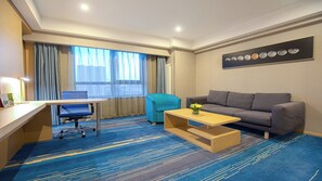 A hotel room with a desk, a sofa, a chair, a coffee table, and a large window with curtains. - Holiday Inn Express Chifeng Hongshan by IHG (Chifeng)