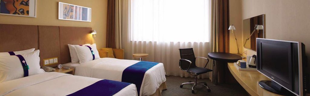 A hotel room with two beds, a desk with a chair, a television, and a window with curtains.