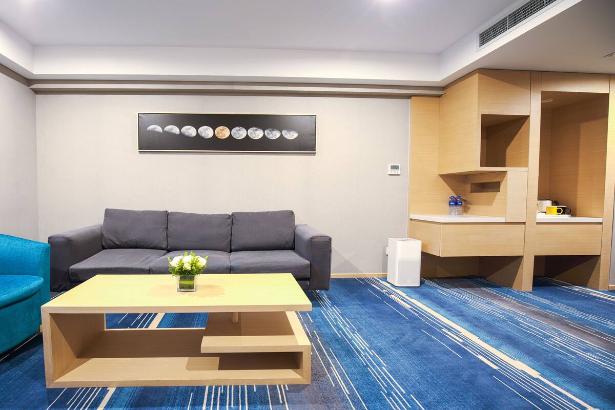 Ein modernes Hotelzimmer mit einem grauen Sofa, einem blauen Sessel, einem Holztisch und einem Wandbild mit den Mondphasen.