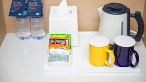 A hotel room's minibar setup with bottled water, coffee maker, tea bags, and two mugs.