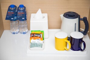 Minibar i et hotelværelse med vand på flaske, kaffemaskine, teposer og to kopper.