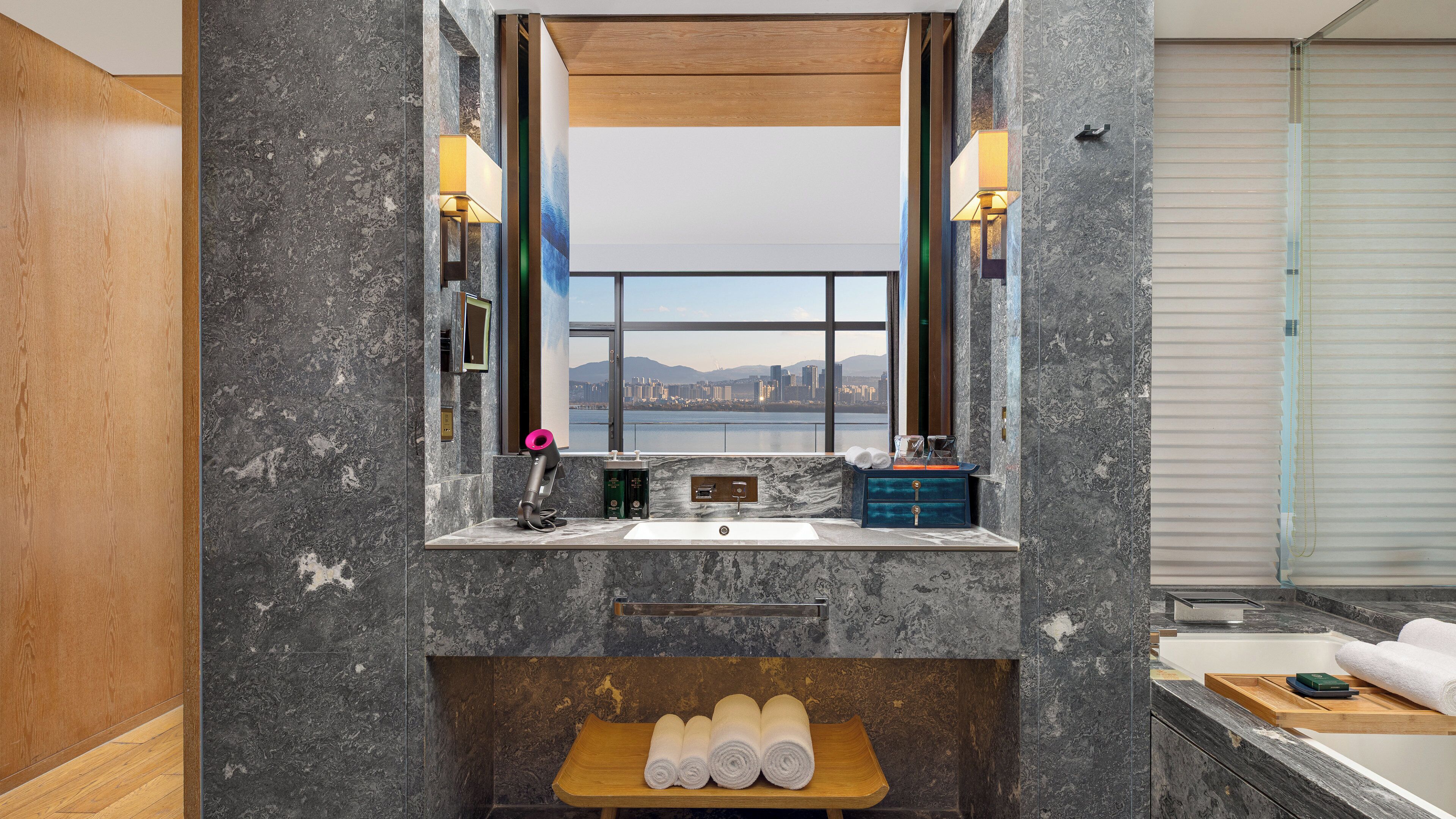 A bathroom with a large mirror, a sink, and a view of a cityscape.