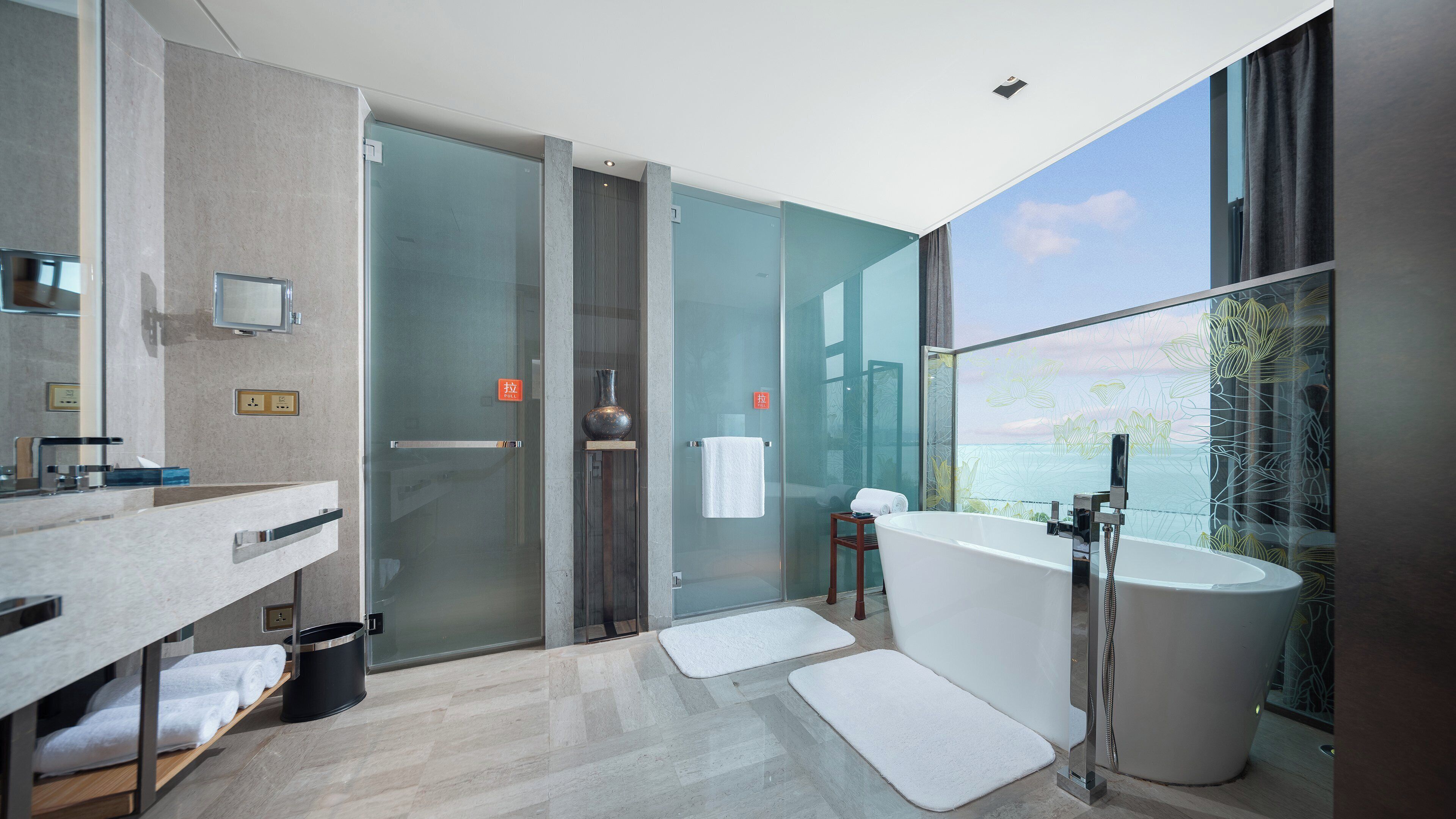 Une salle de bain moderne dotée d’une douche à parois de verre, d’une baignoire sur pieds et d’une grande fenêtre offrant une vue sur l’extérieur.