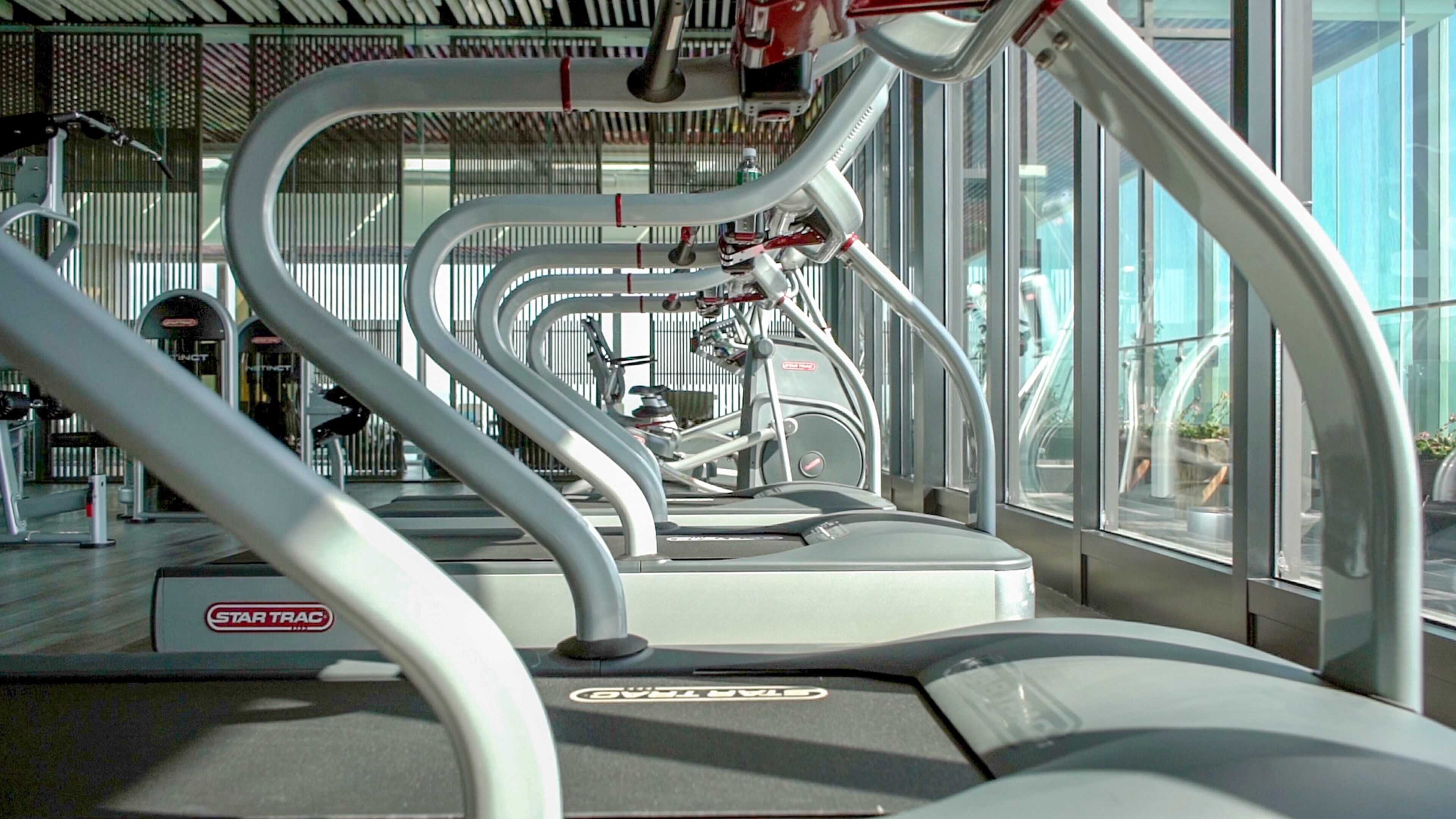 A StarTrac treadmill with a metallic frame, a control panel, and a windowed wall in the background.