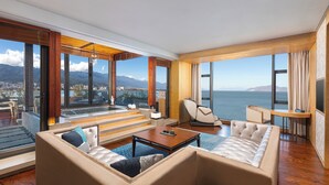Ein geräumiges Wohnzimmer mit einem großen Fenster, das Meer und Berge zeigt.