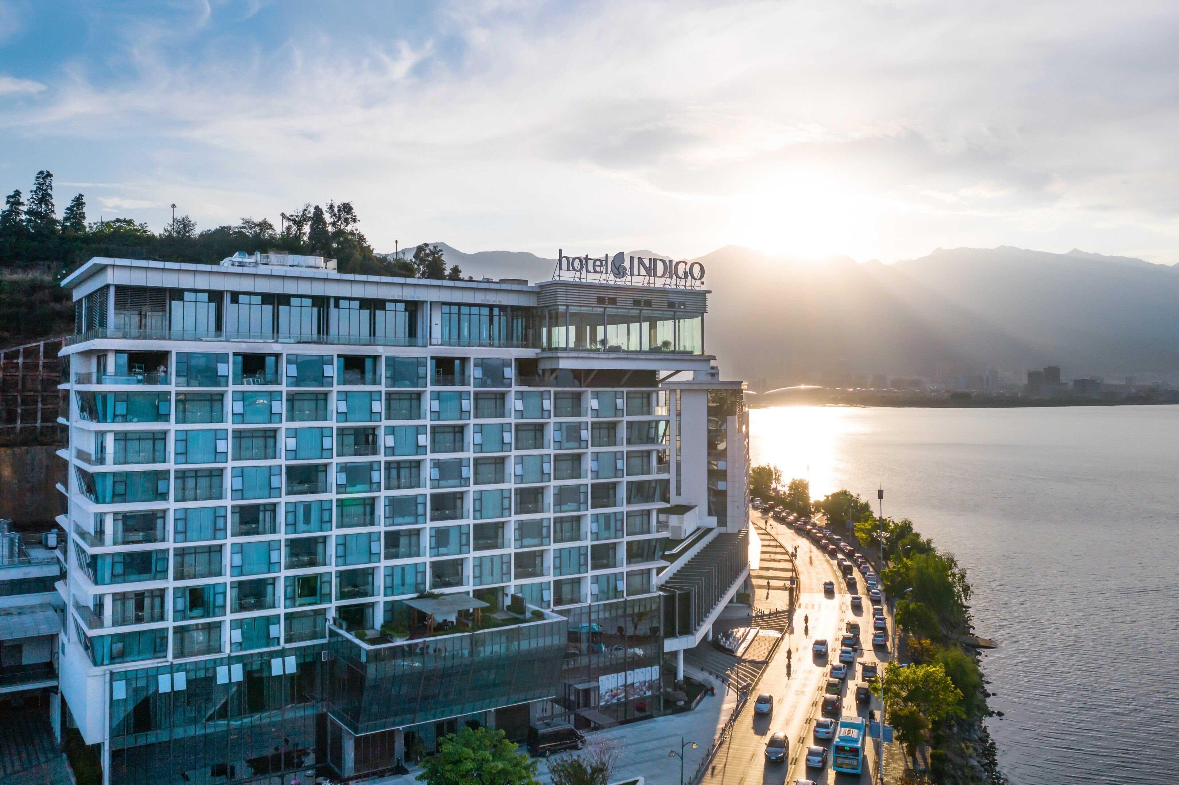Un hotel moderno con varios pisos, un letrero destacado que dice "hotel INDIGO" y vista al agua.