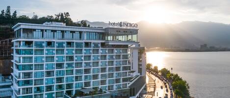 Un hotel moderno con varios pisos, un letrero destacado que dice "hotel INDIGO" y vista al agua.