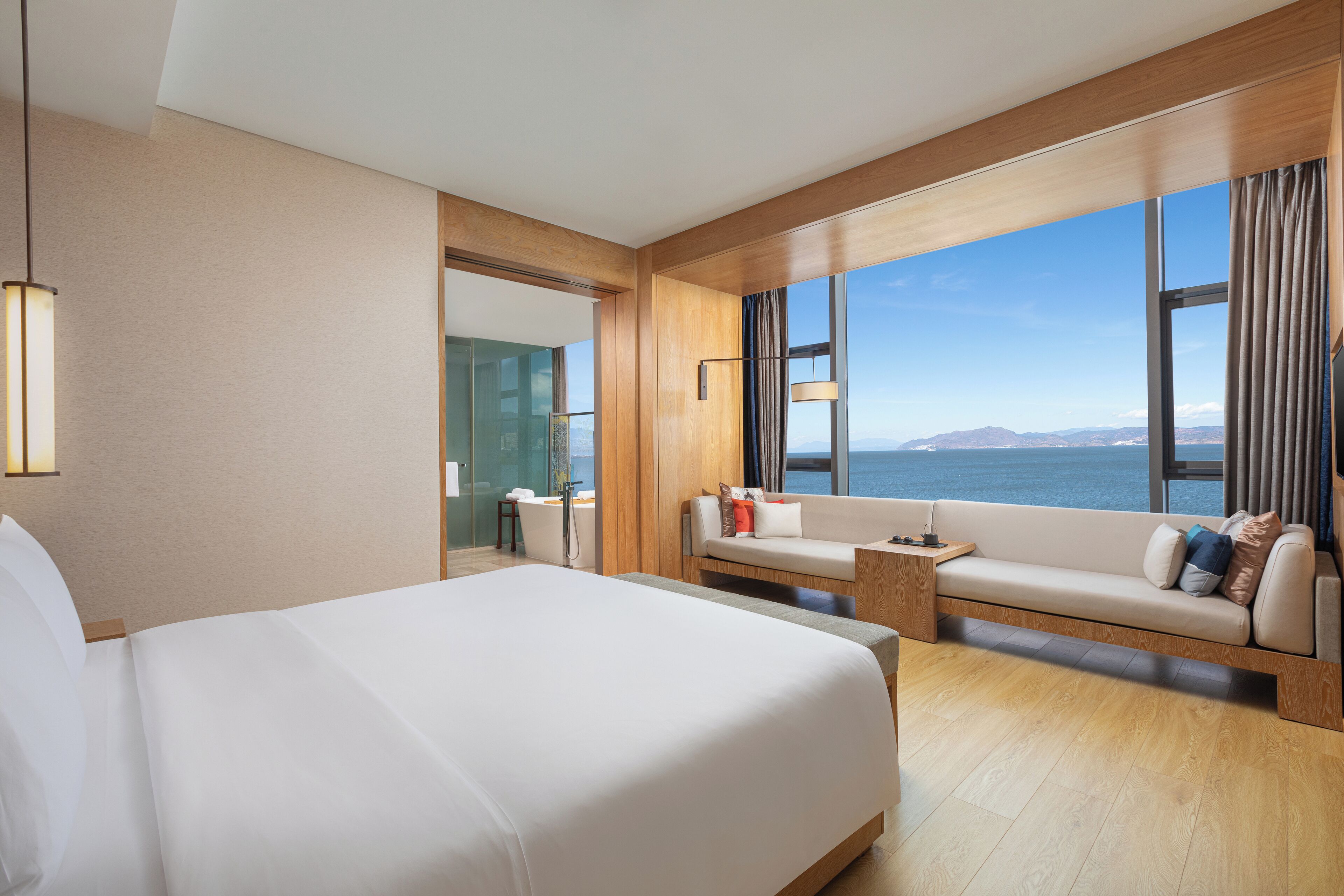A hotel room with a large bed, a sofa, a small table, and a view of the ocean.