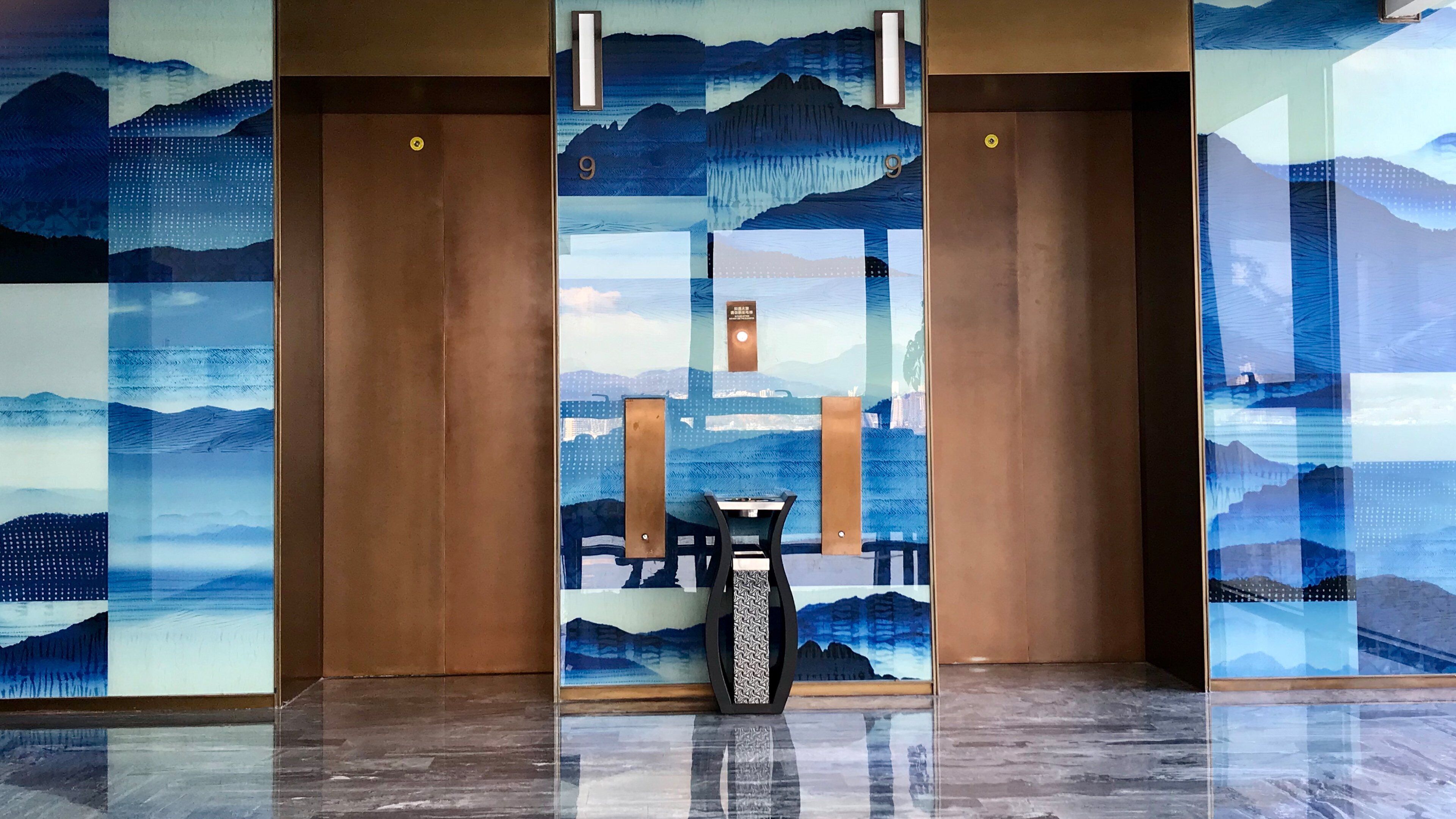 A hallway with three elevators, each with a wooden door and a blue mural depicting a mountainous landscape.