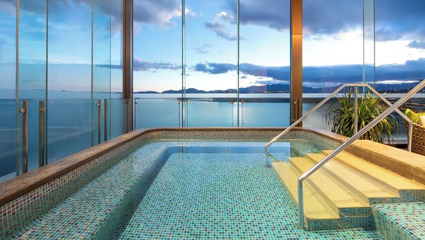 Ein Pool mit Blick auf das Meer und die Berge, umgeben von Glaswänden.
