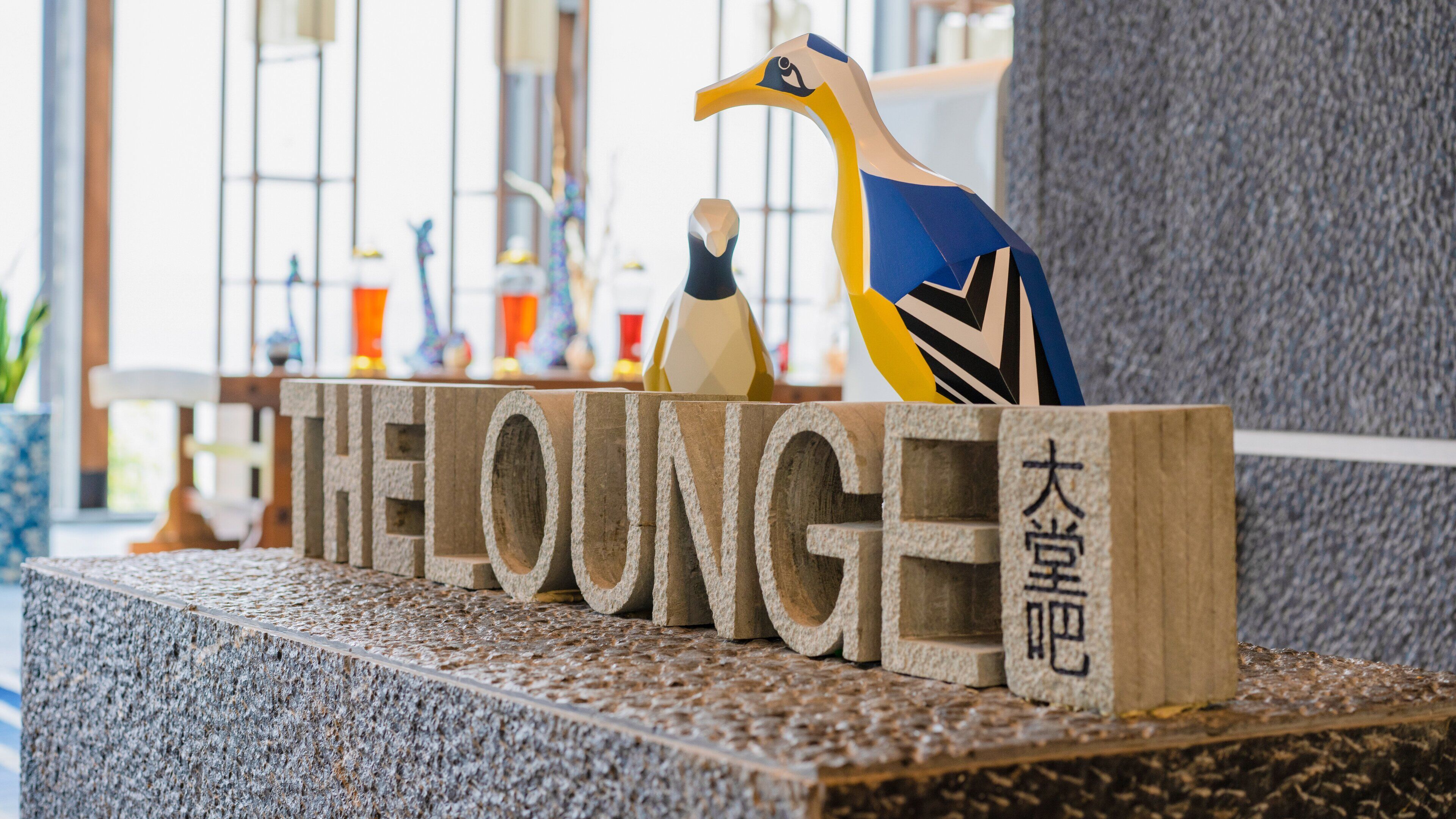 En träskylt med ordet ”THE LOUNGE” och en dekorativ fågelstatyett.