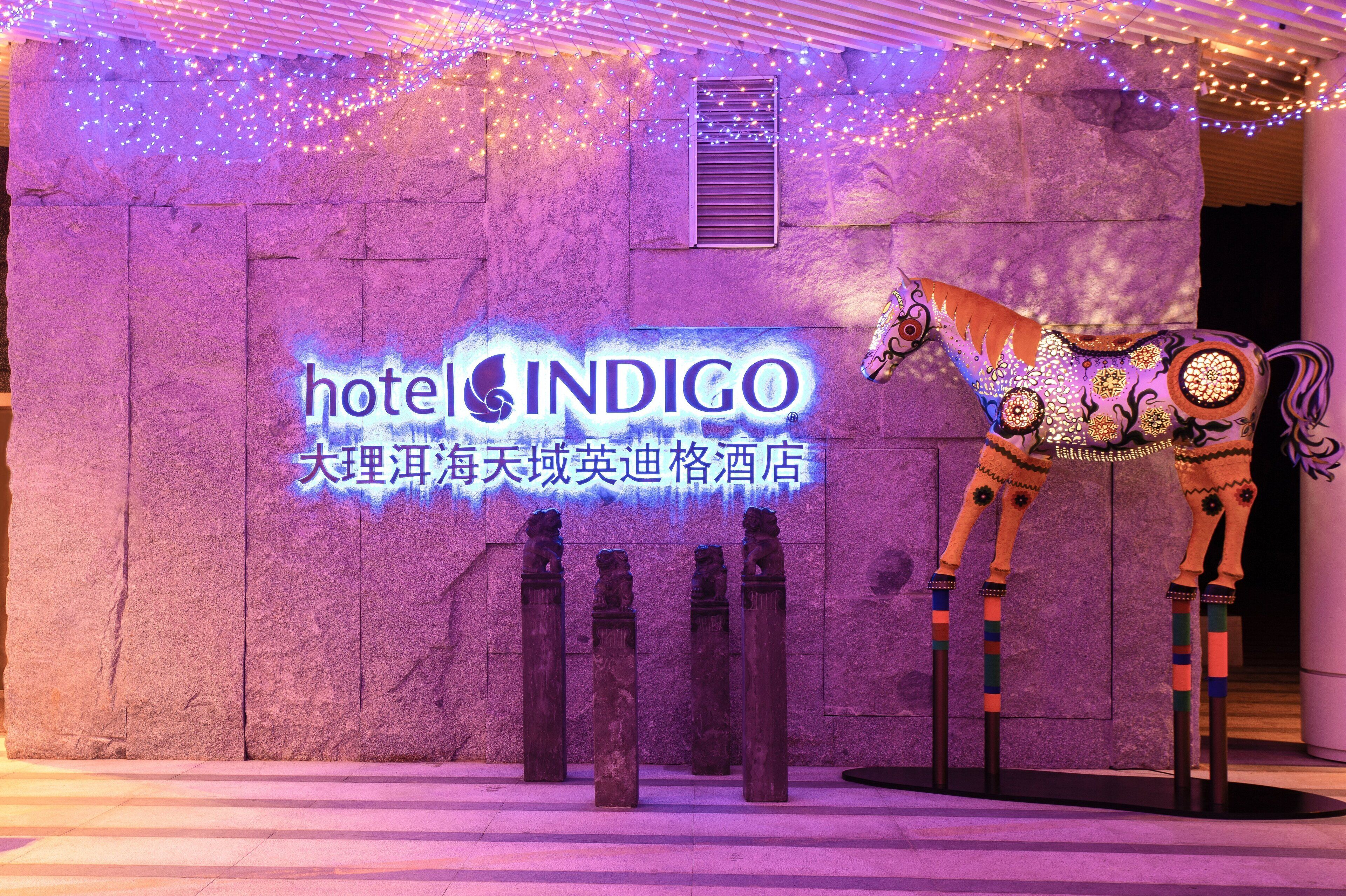 A stone wall with a neon sign for 'hotel INDIGO' and a decorative horse statue.