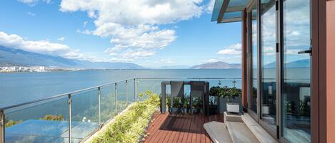 A balcony with a view of a lake and mountains, featuring a glass railing and potted plants.