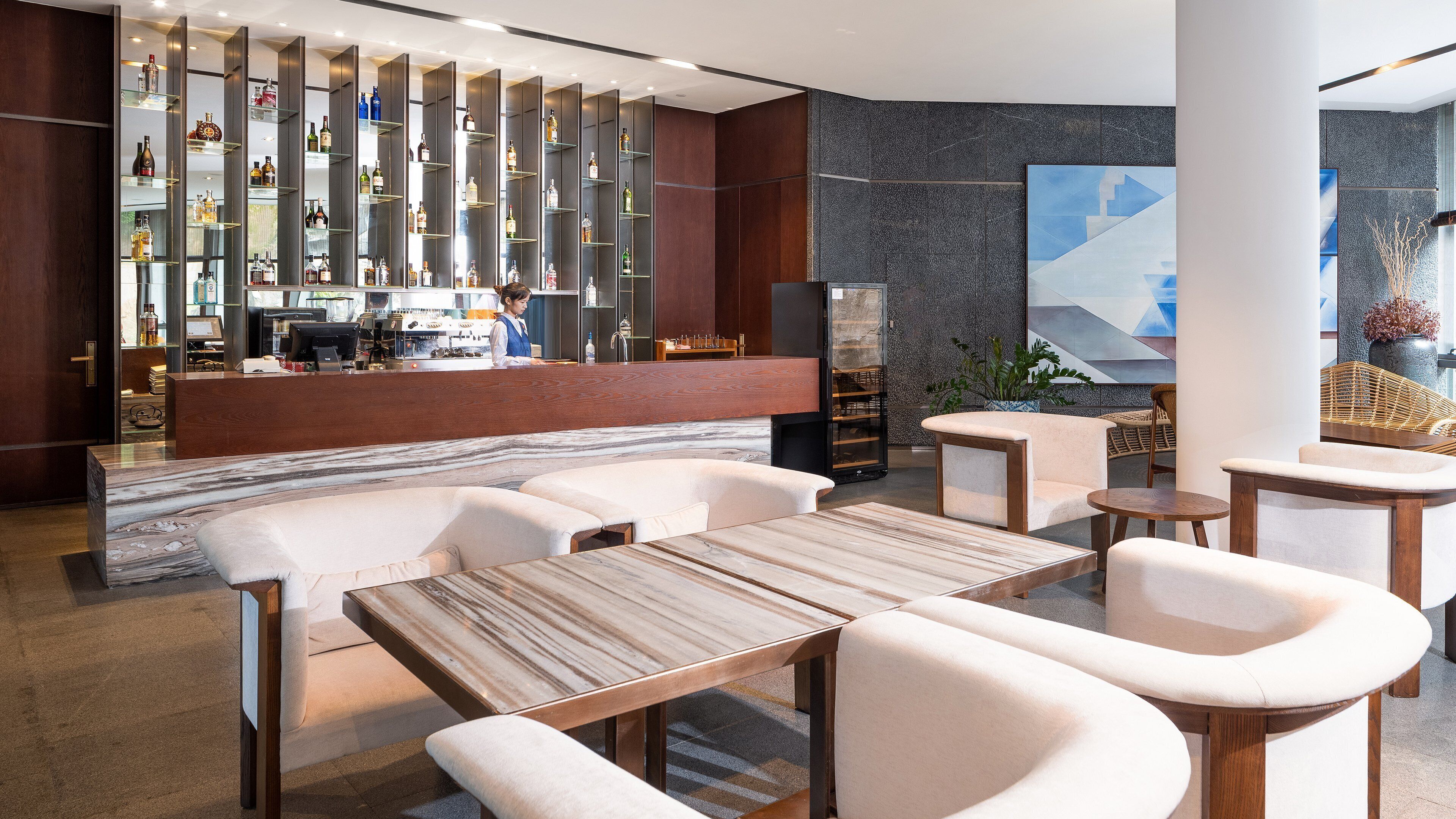 A modern bar area with a long counter, shelves with bottles, and a seating area with sofas and tables.