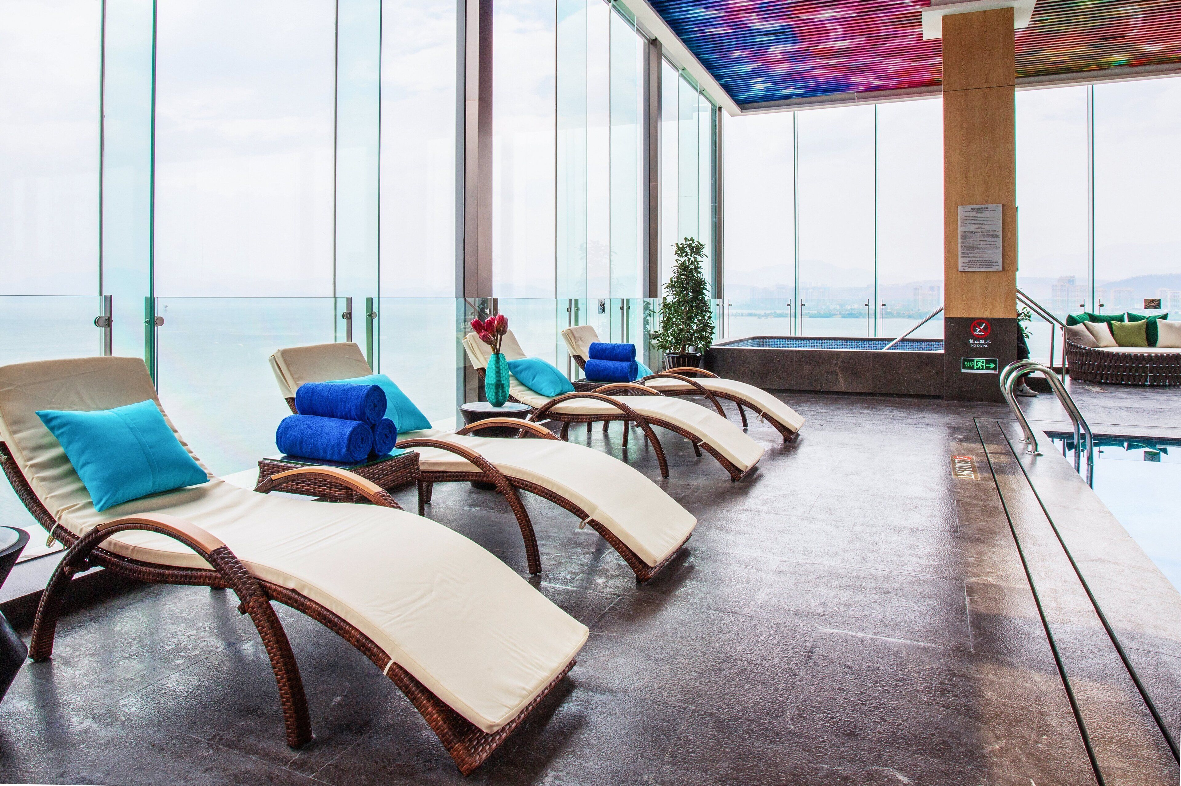 A sun lounge with wicker chairs and cushions, a pool, and a city view.
