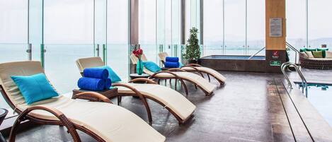 Un sillón de sol con sillas de mimbre y cojines, una piscina y vistas a la ciudad.