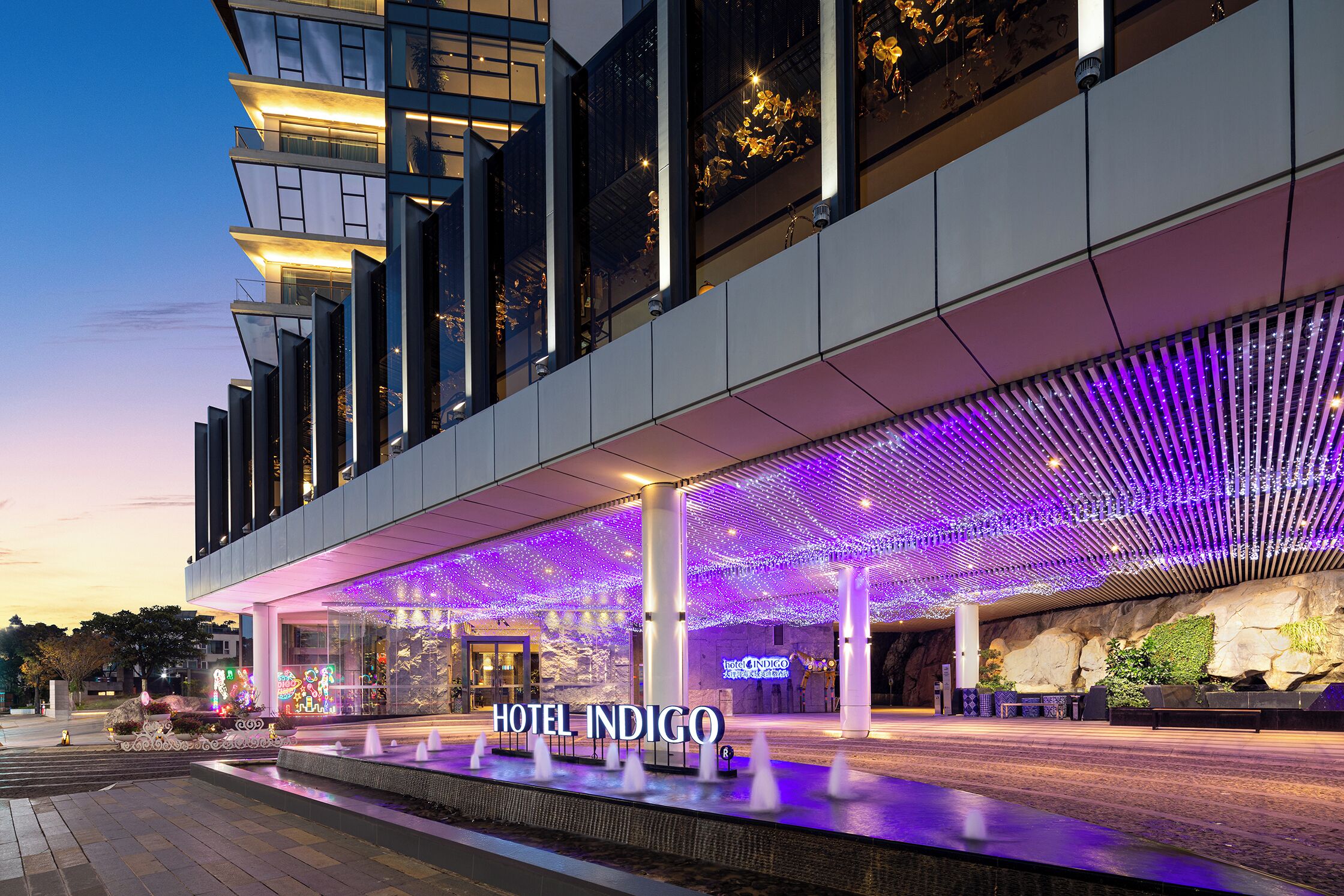 A modern hotel with a prominent entrance, a covered outdoor area with a patterned ceiling, and a visible sign for Hotel Indigo.