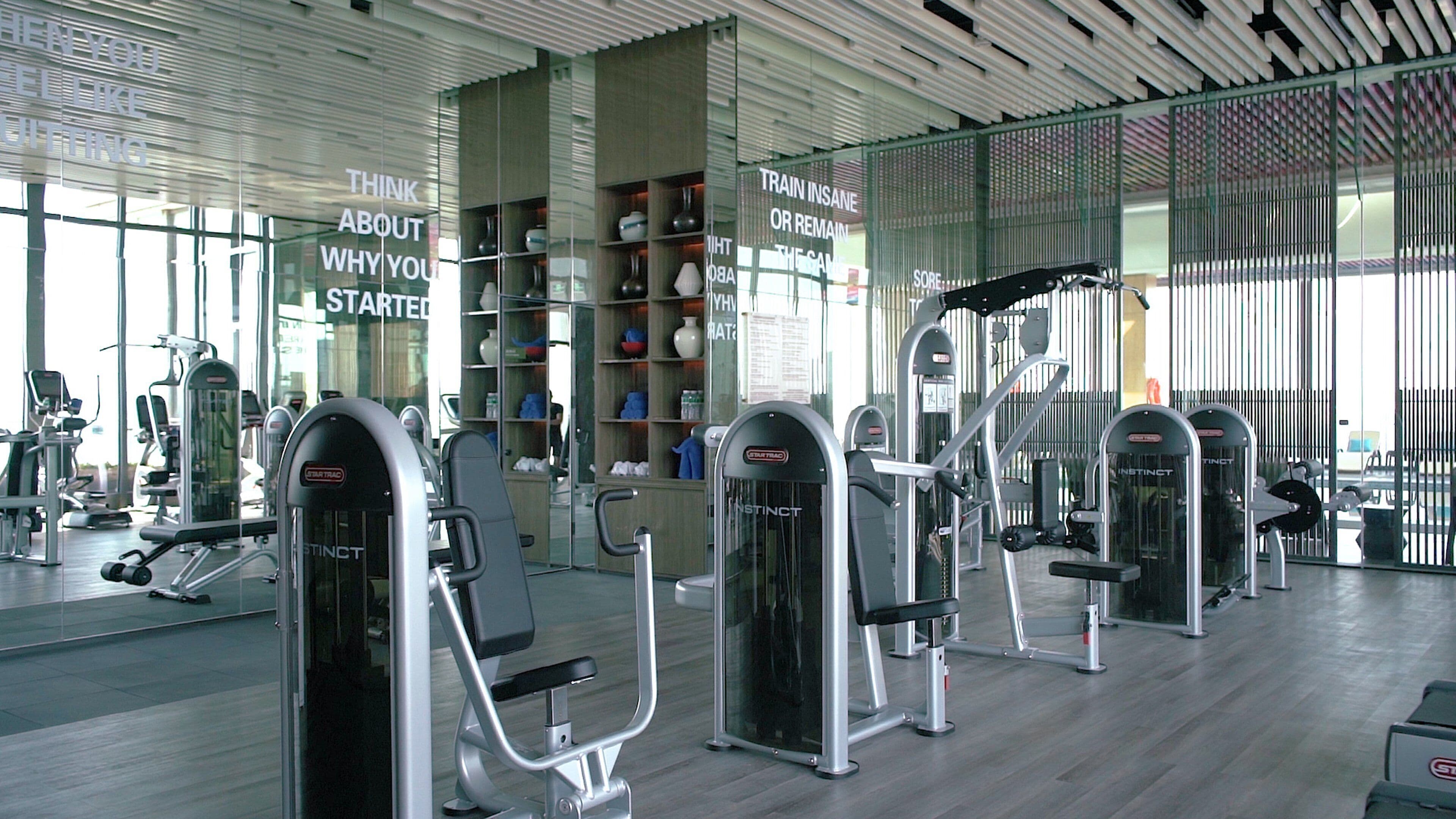 Un gimnasio moderno con diversas máquinas de ejercicio, ventanas amplias y citas motivacionales en las paredes.