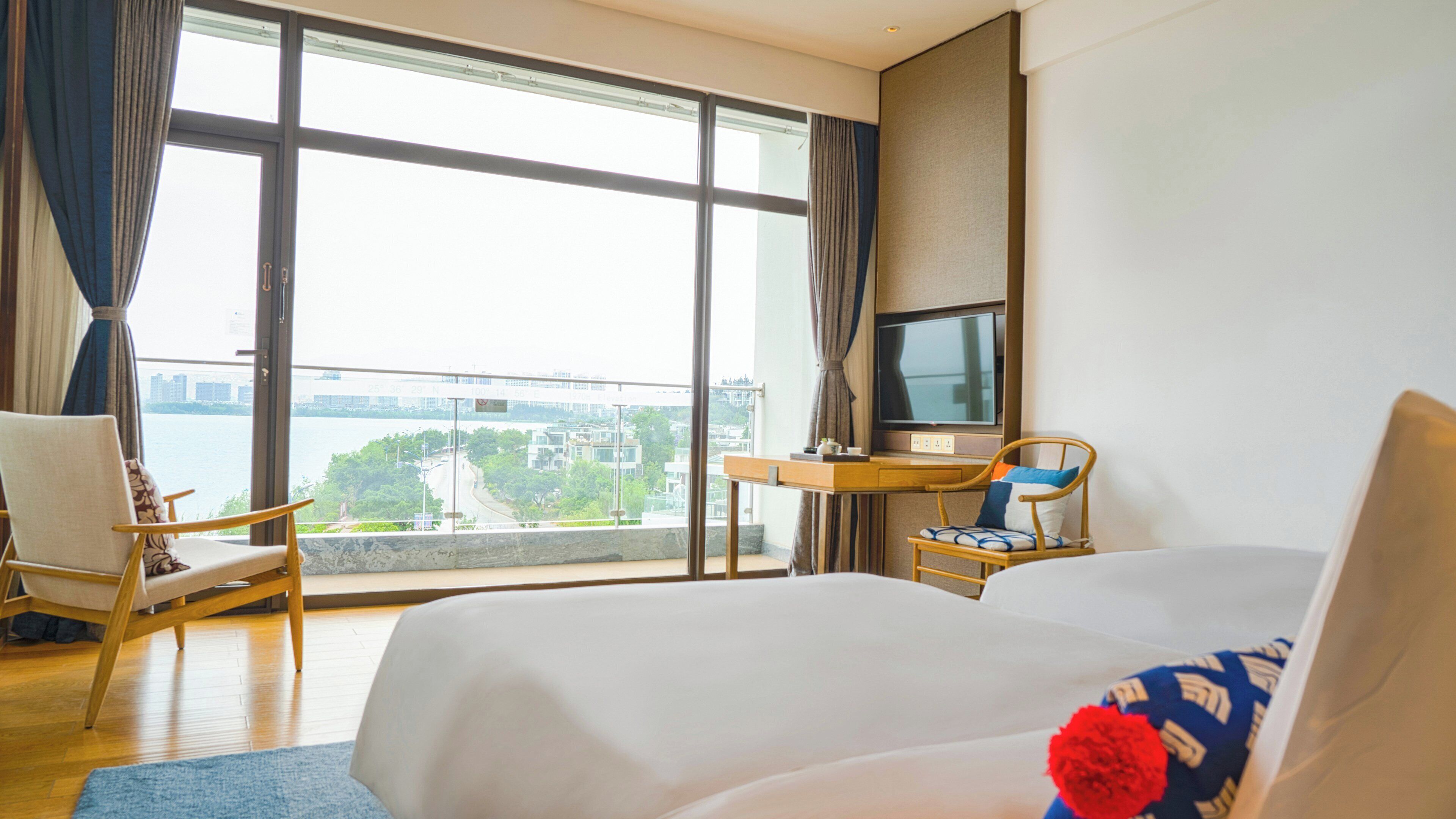 A hotel room with a large window, a bed, a desk, and a chair.