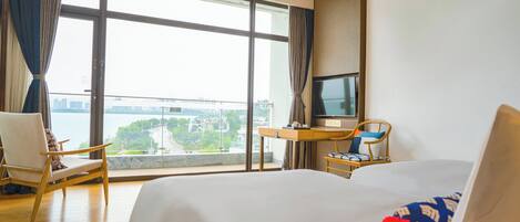 A hotel room with a large window, a bed, a desk, and a chair.