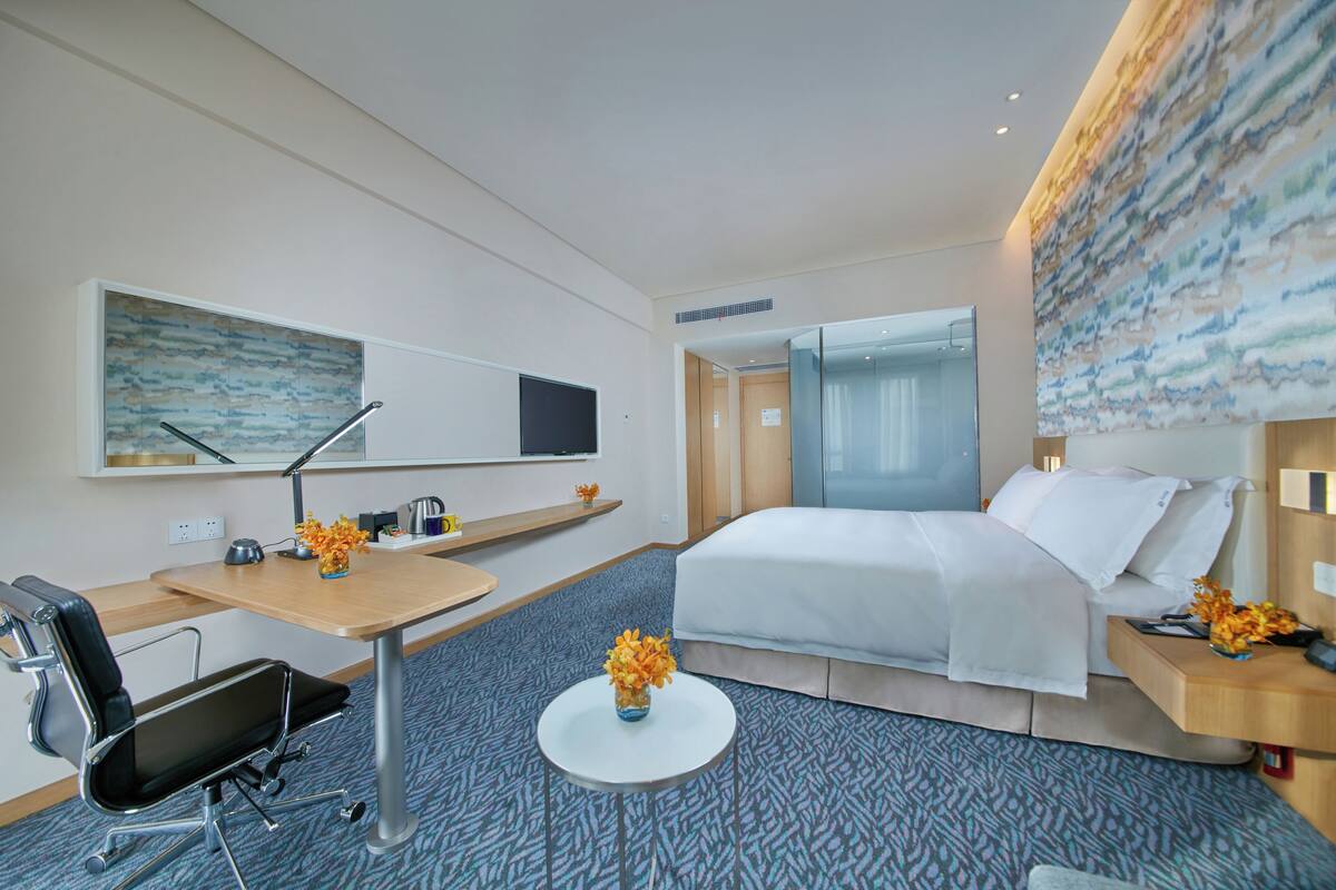 Ein Hotelzimmer mit einem Bett, einem Schreibtisch, einem Stuhl, einem kleinen Tisch und einer Vase mit Blumen.