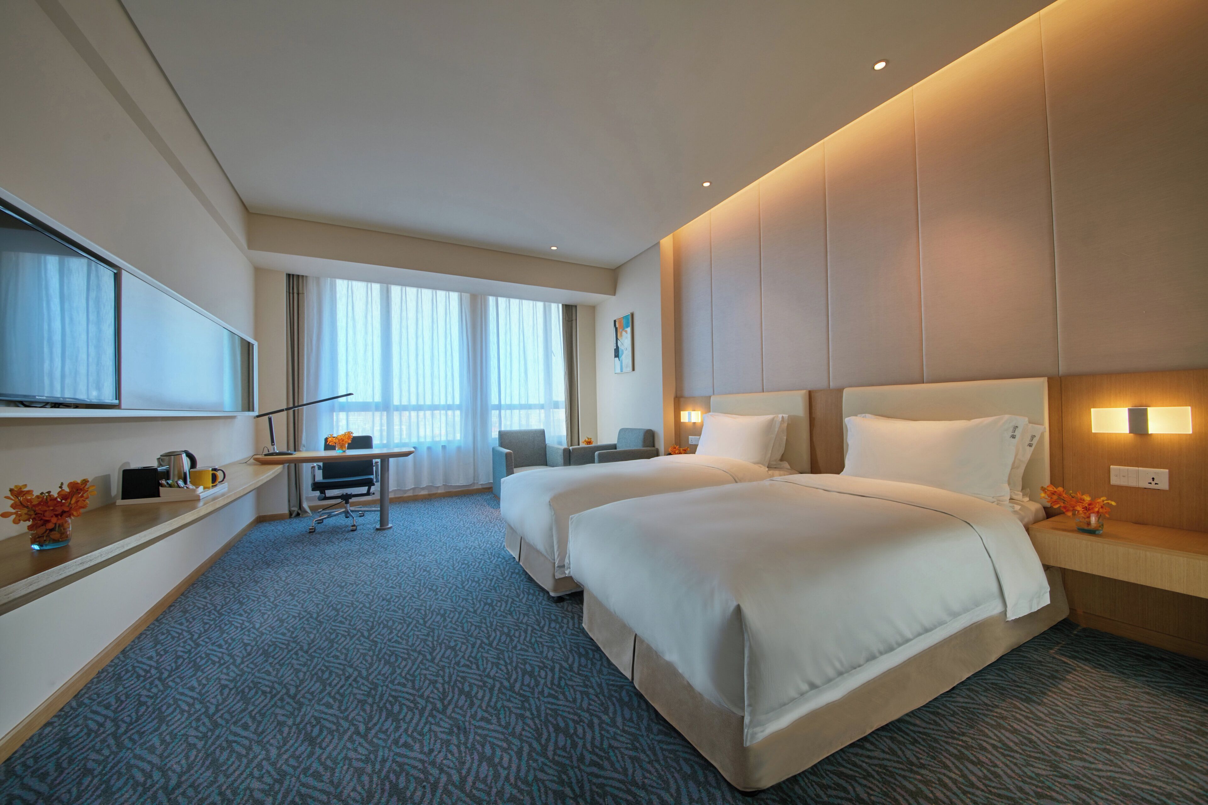 A hotel room with two beds, a desk, a chair, a TV, and a large window.