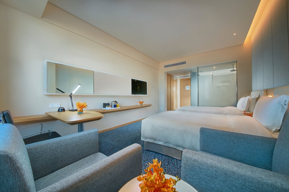 Ein modernes Hotelzimmer mit einem großen Bett, einer Couch, einem Schreibtisch mit Lampe und einem Fernseher.