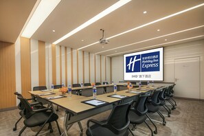 A conference room with a long table, chairs, water bottles, and a projector screen displaying a hotel name. - Holiday Inn Express Nantong Textile City by IHG (Nantong)