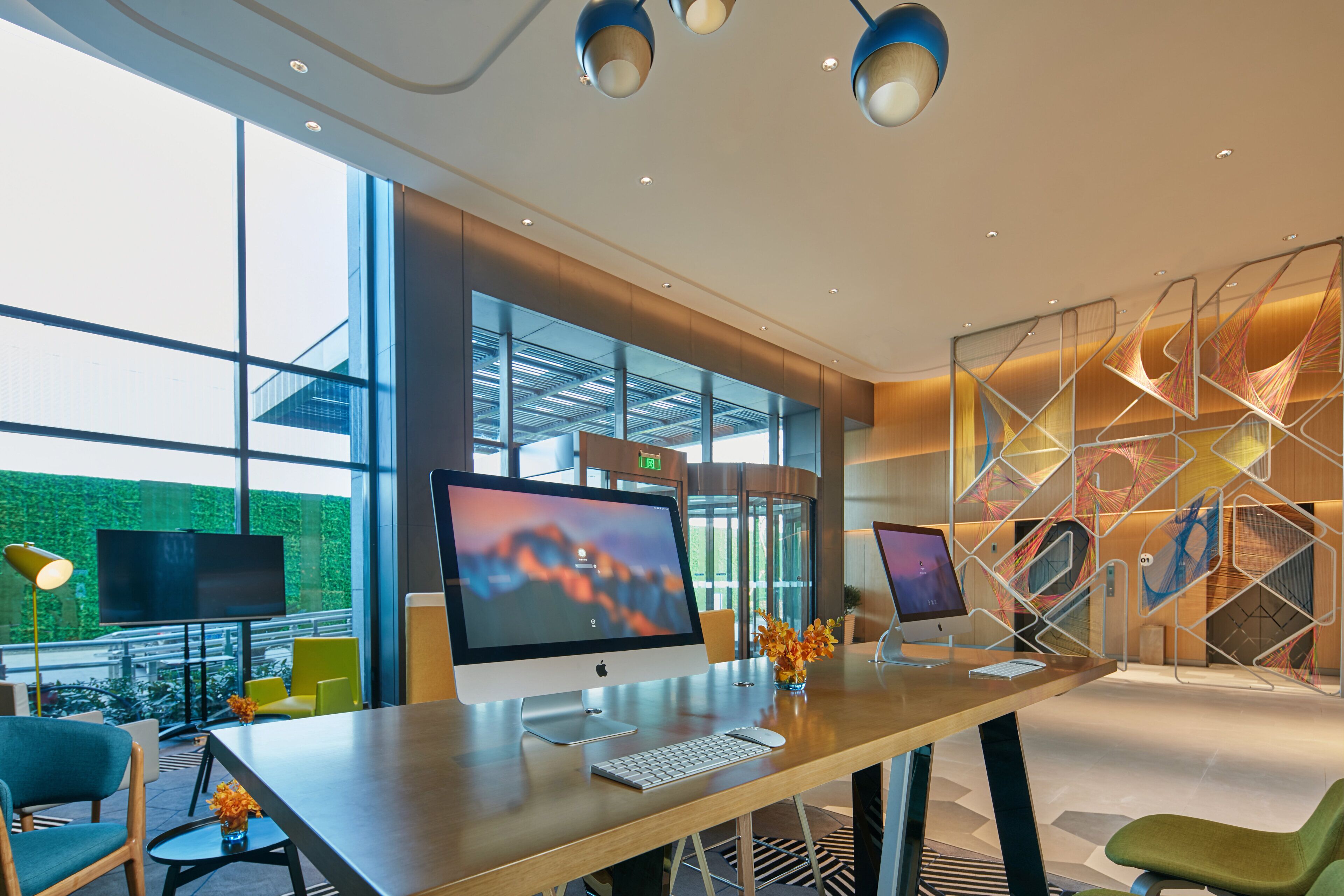 A modern office space with two desktop computers, a large window, and a decorative wall.