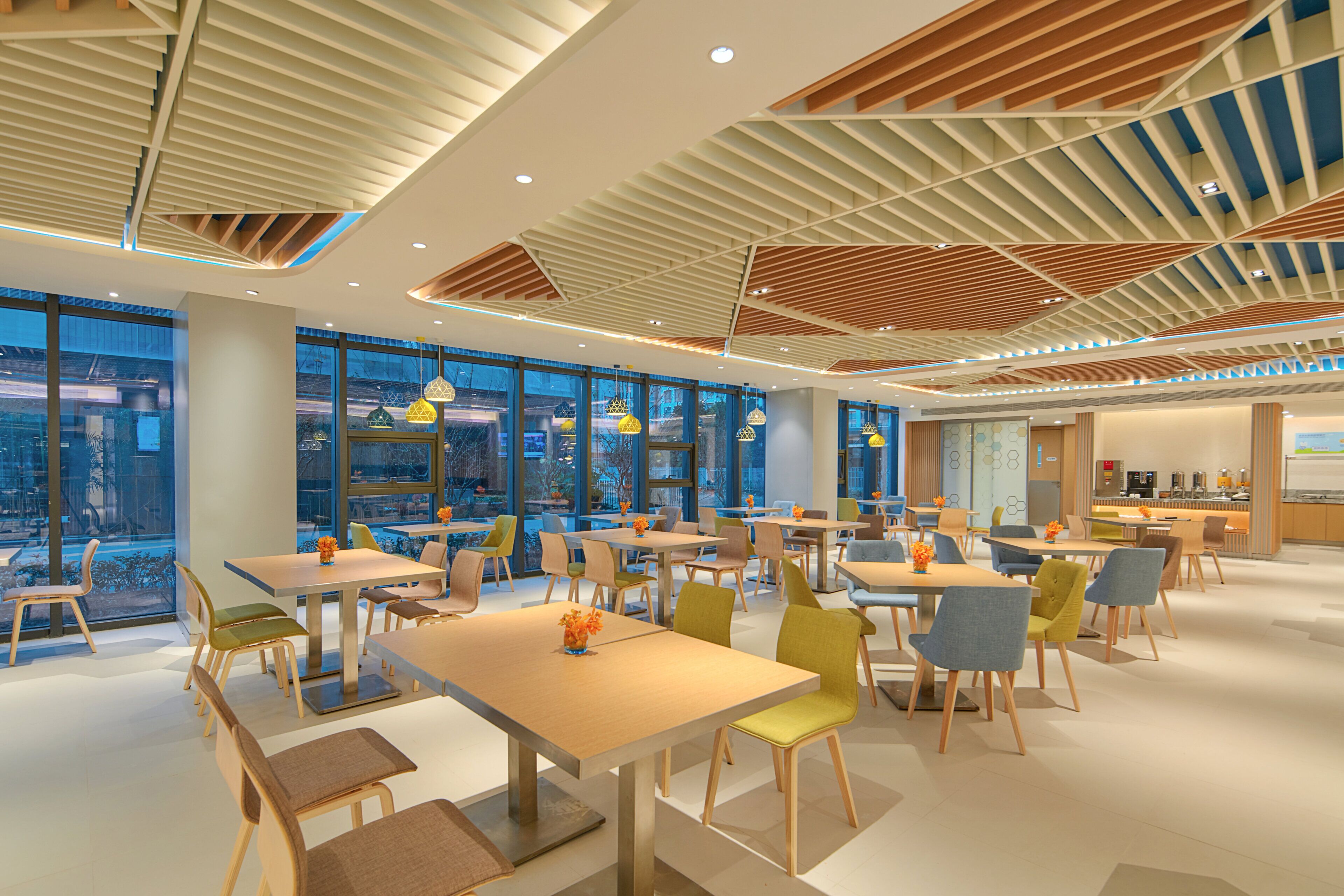 Un comedor moderno con mesas y sillas, ventanas amplias y un techo con listones de madera.