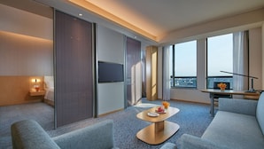 A modern hotel room with a large window, a flat-screen TV, a sofa, a coffee table, and a small table with a vase of flowers. - Holiday Inn Express Nantong Textile City by IHG (Nantong)