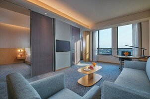 Habitación de hotel moderna con sofá, una mesita con un florero, televisor de pantalla plana y un ventanal con vistas a la ciudad.