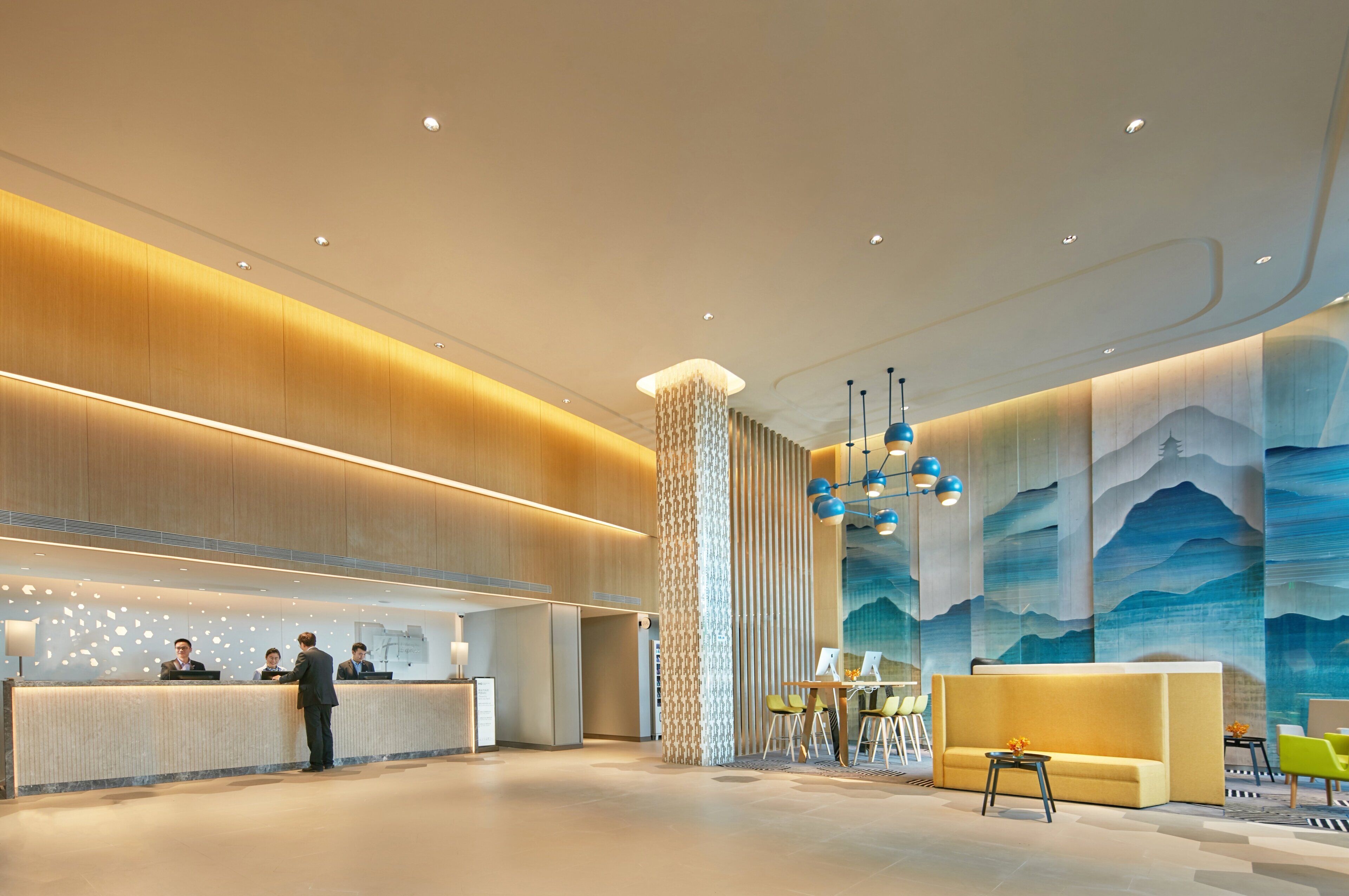A modern hotel lobby with a reception desk, seating area, and decorative wall art.
