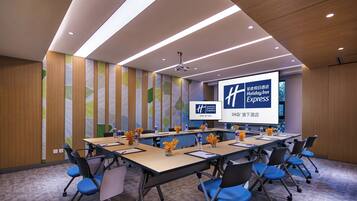 A conference room with a long table, chairs, a projector screen, and a presentation about Holiday Inn Express.