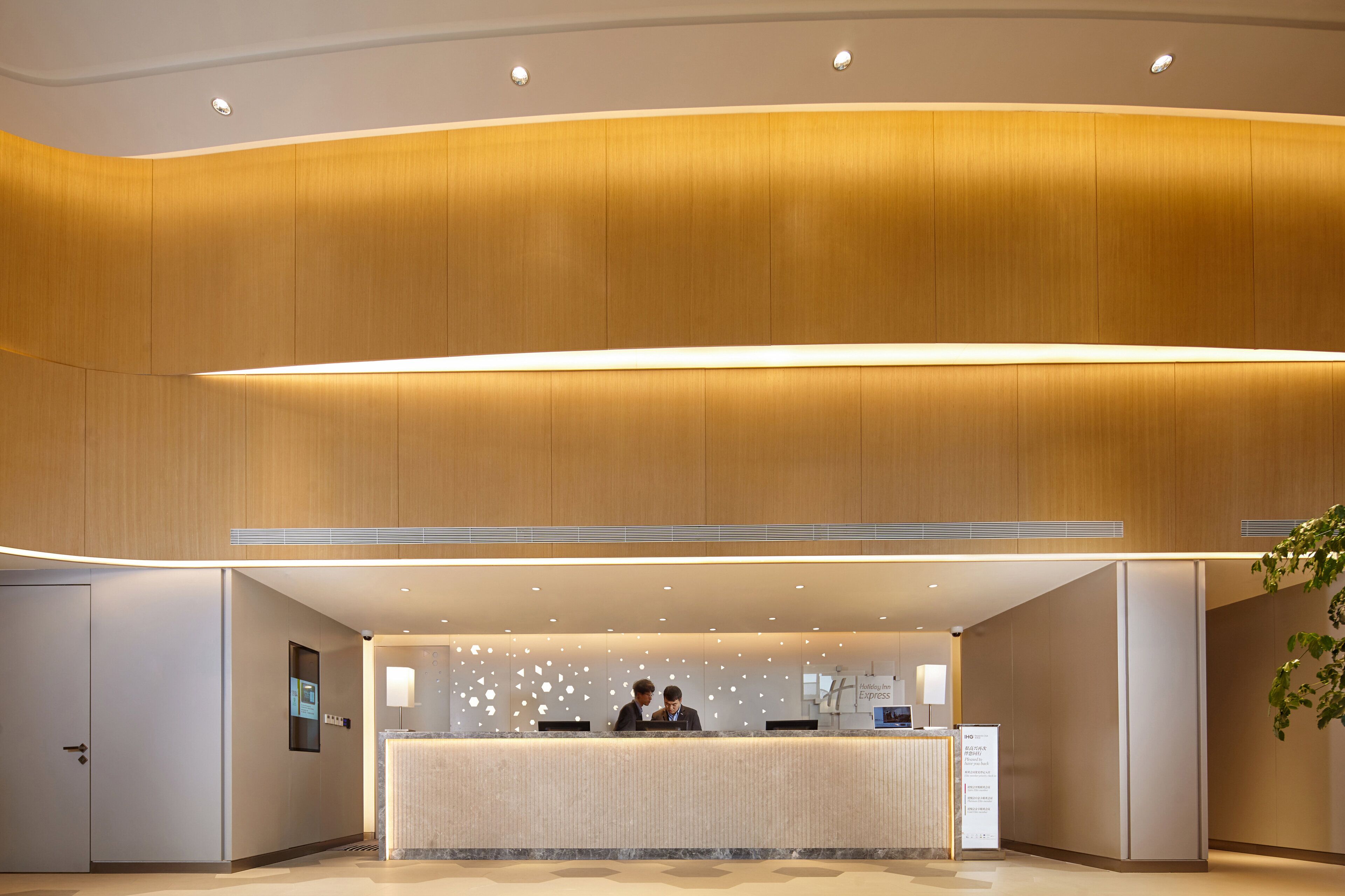 A hotel reception area with a modern design, featuring a reception desk, a digital information screen, and a reception counter.
