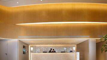 A hotel reception area with a modern design, featuring a reception desk, a digital information screen, and a reception counter.