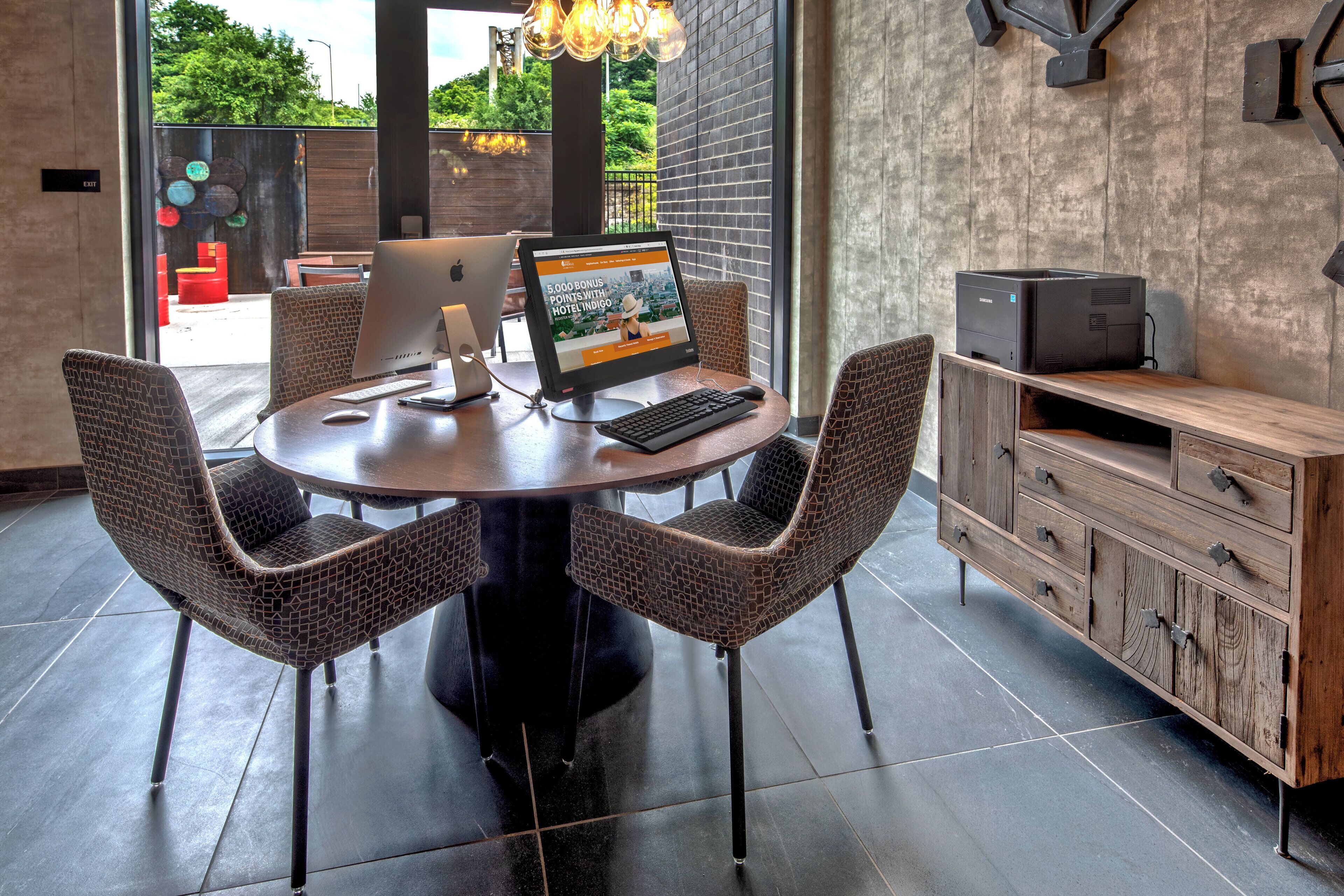 A modern office space with a round table, four chairs, a desktop computer, a monitor, a keyboard, a mouse, and a printer.