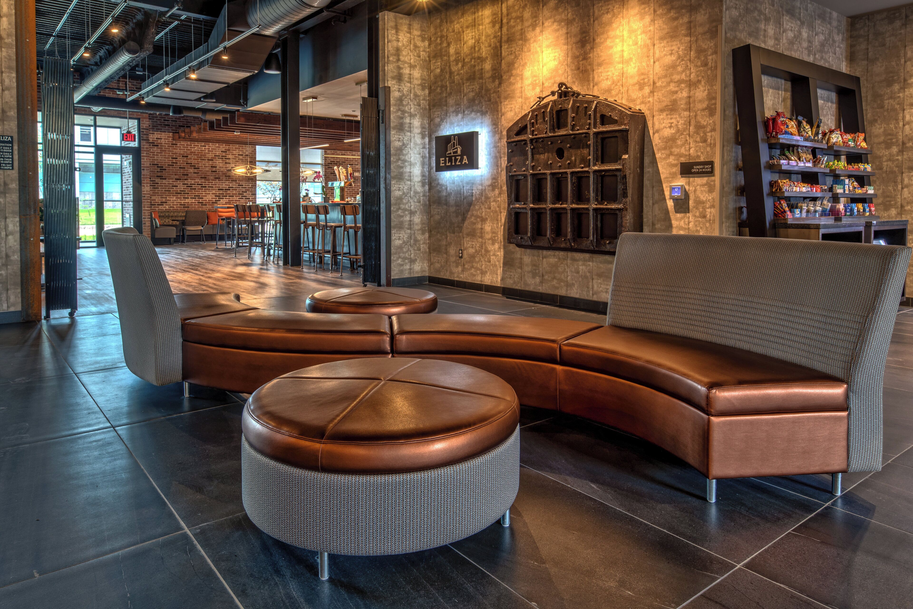 A modern lounge area with a leather sofa, a round ottoman, and a bar area with snacks.