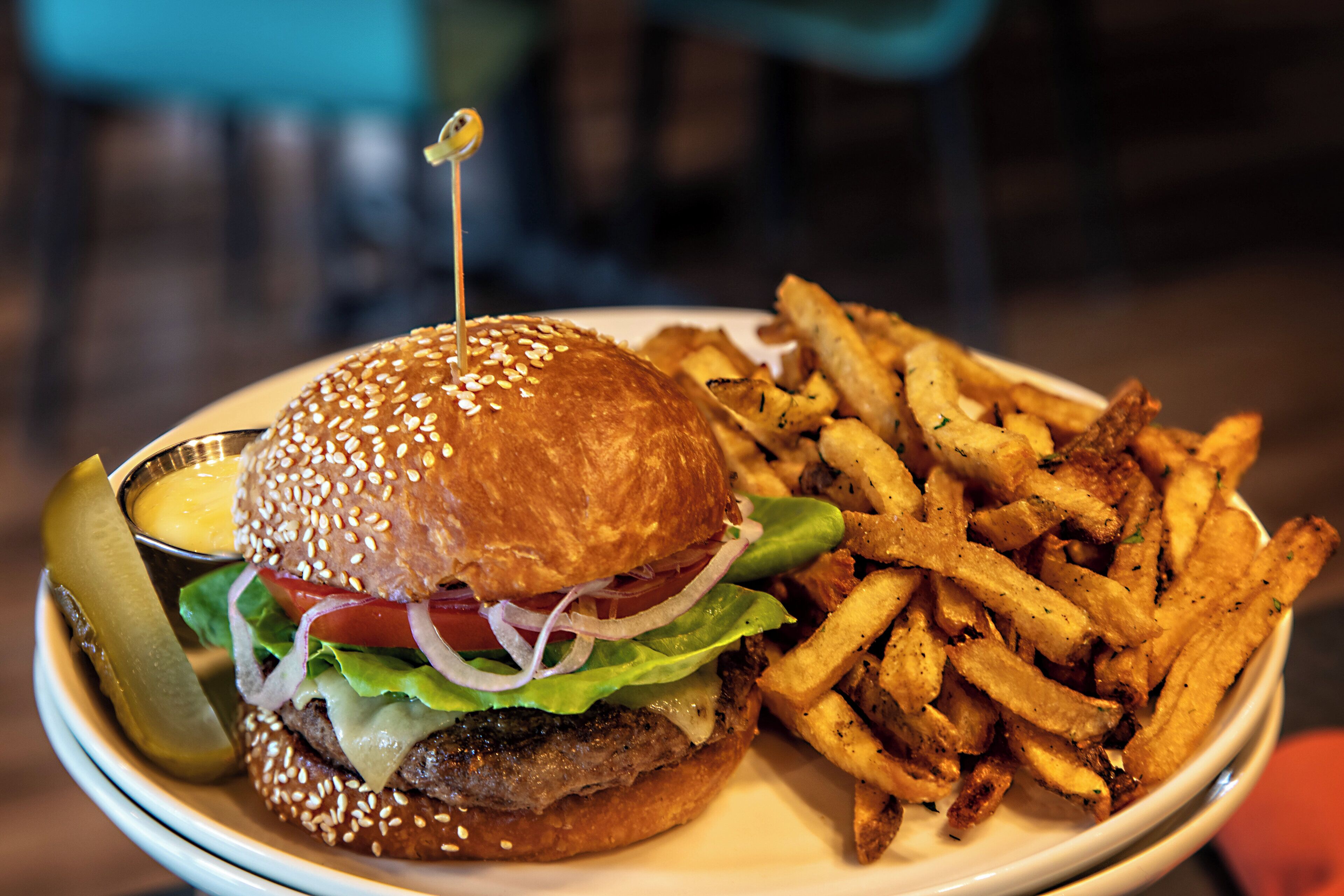 Un plat amb una hamburguesa, patates fregides i un cornichó.