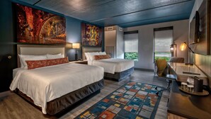 A hotel room with two beds, a large abstract painting, a view of greenery, and a desk with a lamp.
