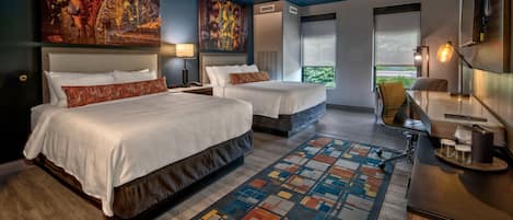 A hotel room with two beds, a large abstract painting, a view of greenery, and a desk with a lamp.