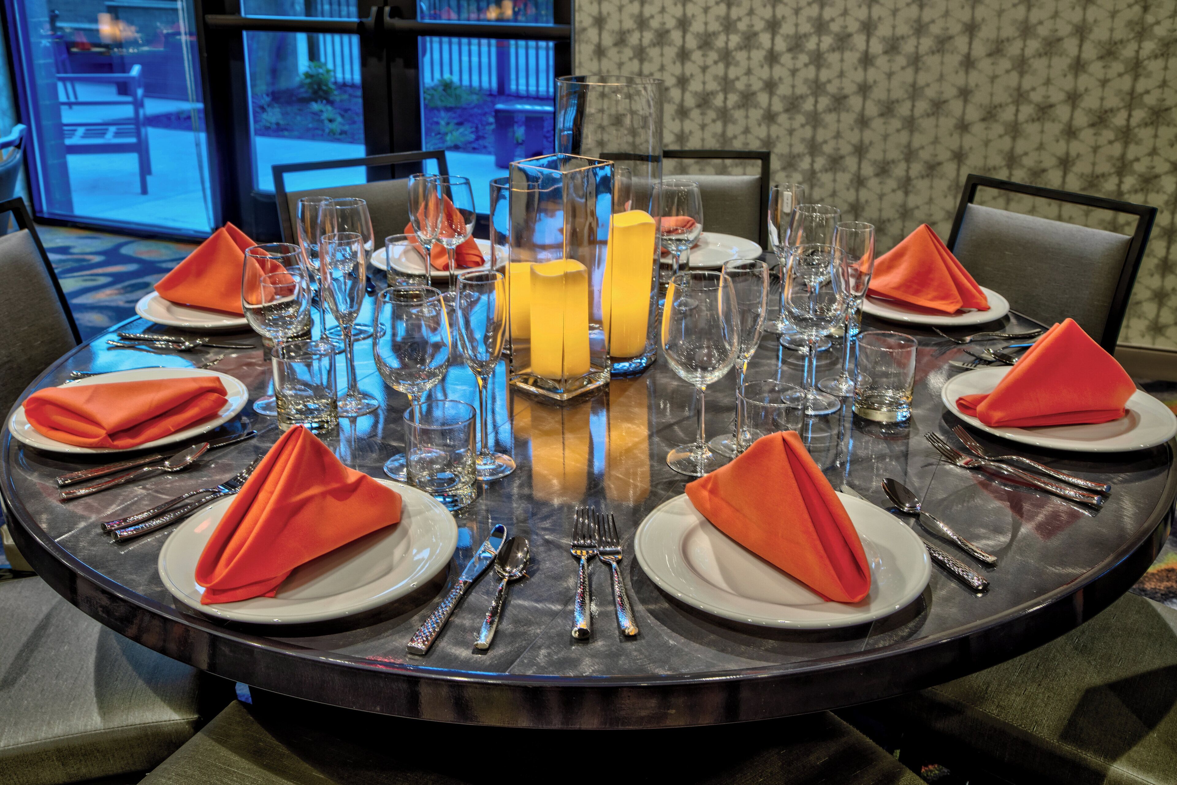 A round dining table set for four with clear glassware, plates, and cutlery.